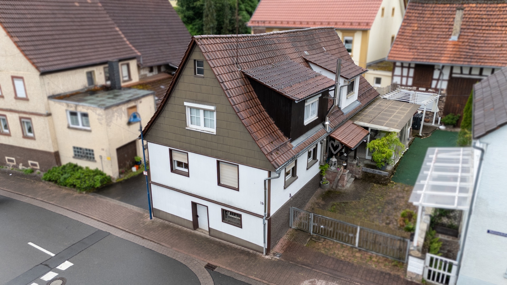 Zweistöckiges Wohnhaus mit braunem Schrägdach und kleinem Innenhof, an einer Straßenkurve gelegen.