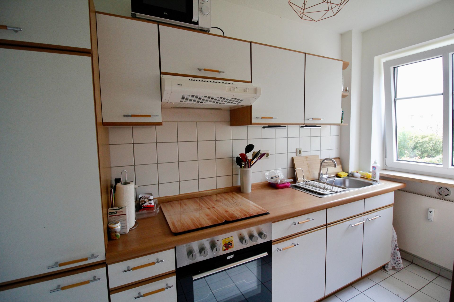 Helle Küche mit weißen Schränken, Elektroherd, Spüle und Fensterausblick.