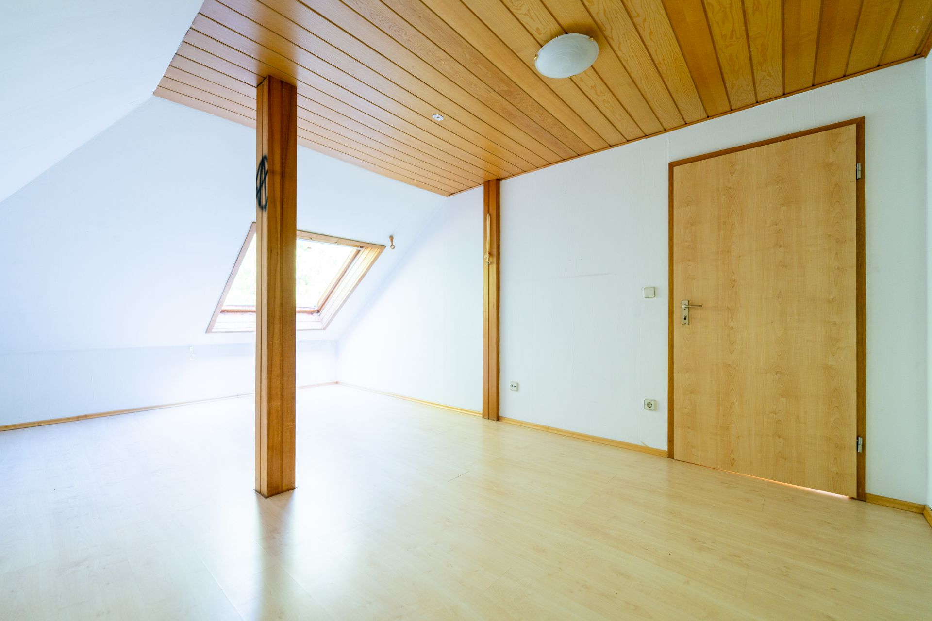 Helles leeres Zimmer mit Holzdecke, Holzboden, Dachfenster und Tür.