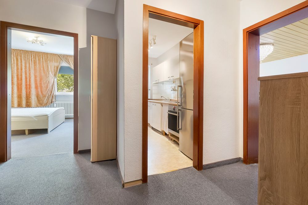 Flur mit Türen zu Schlafzimmer, Küche und weiterem Raum, Teppich und Holzmöbeln.