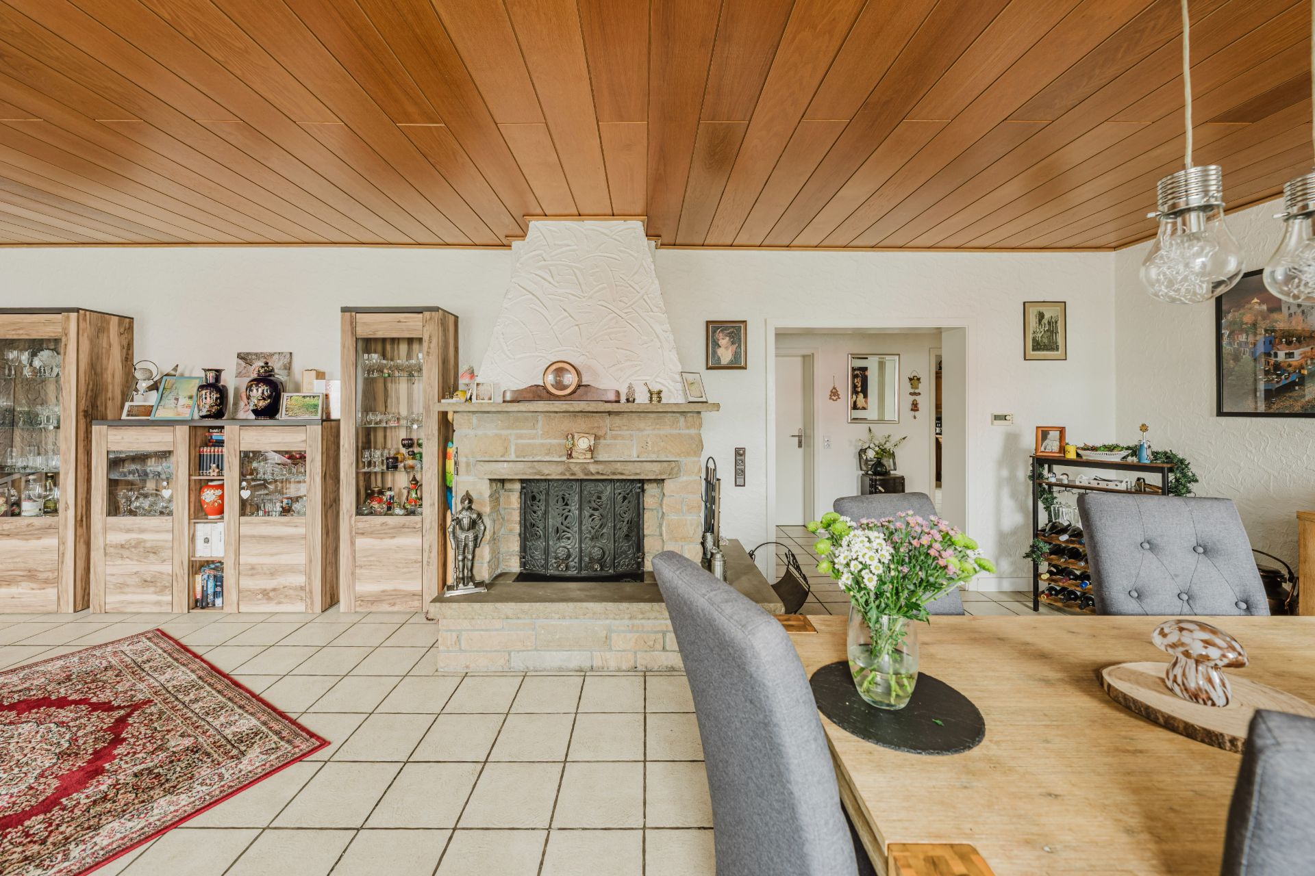 Wohnzimmer mit Kamin, Holzmöbeln, Esstisch und Fliesenboden.