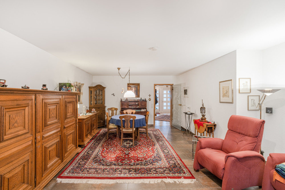 Wohnzimmer mit Holzmöbeln, rundem Tisch, rotem Sessel und orientalischem Teppich.