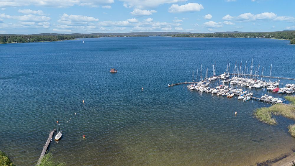 Blick auf einen See mit Bootssteg und mehreren Segelbooten am Ufer.