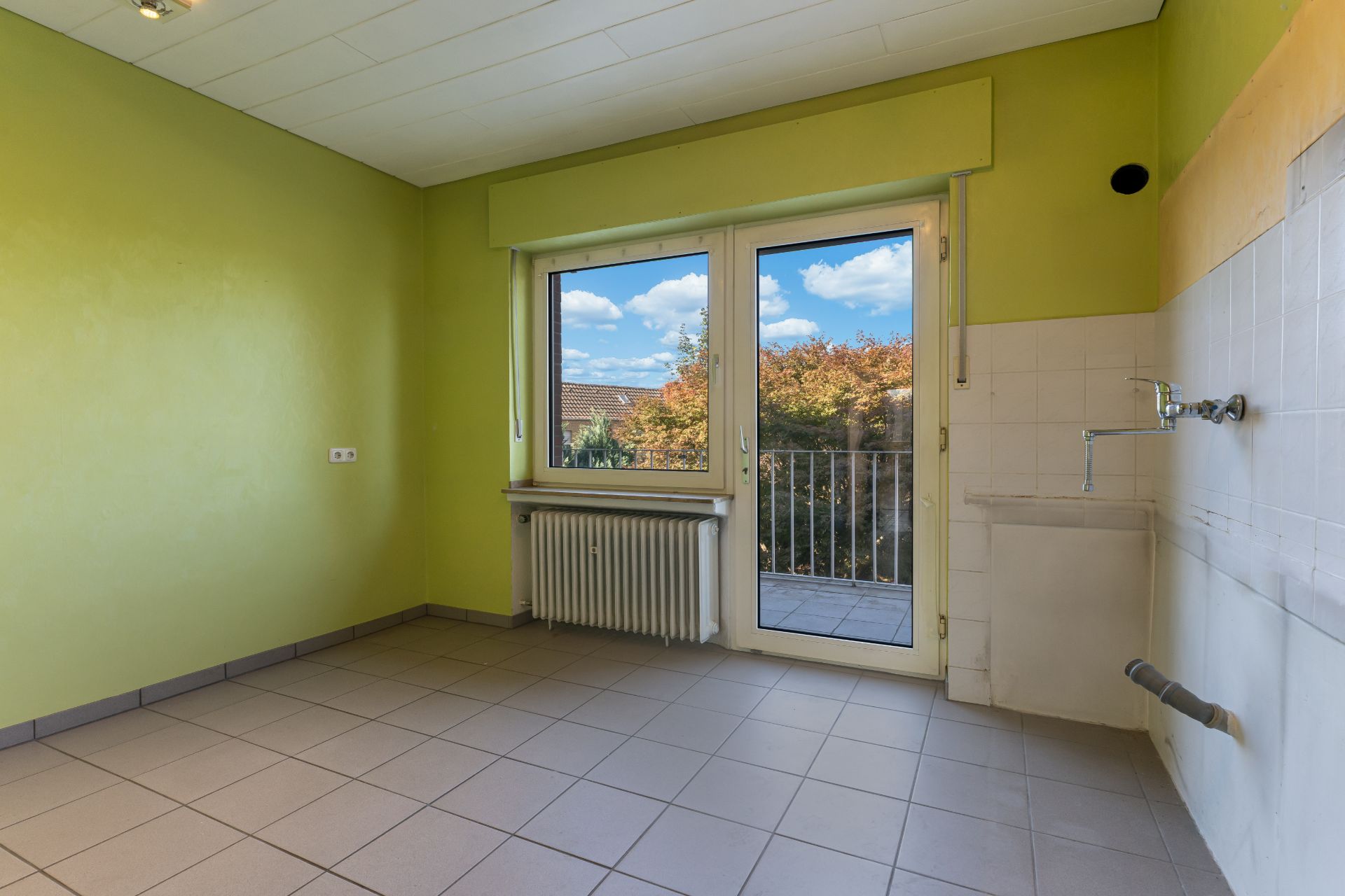 Leerer Raum mit Fliesenboden, grün gestrichenen Wänden und Glastür zum Balkon.