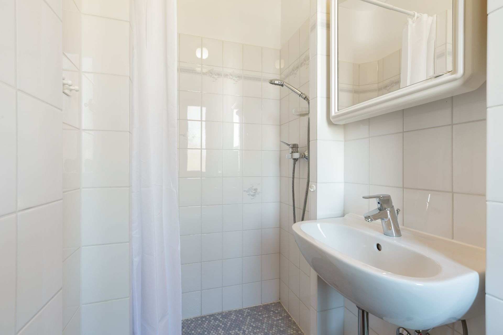 Helles Badezimmer mit Dusche, Waschbecken und Spiegel.
