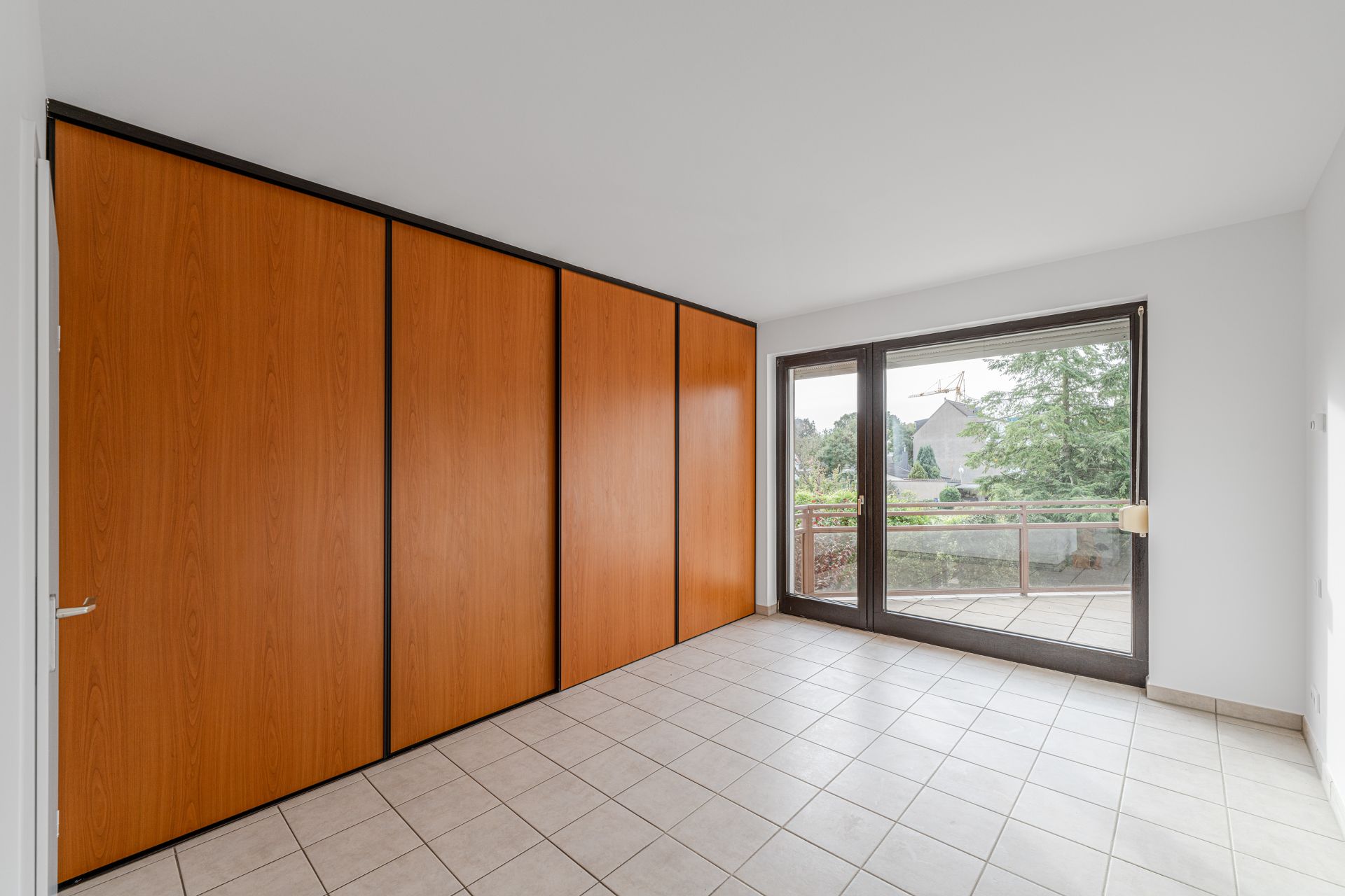 Heller Raum mit großen Einbauschränken, Fliesenboden und Glas-Schiebetür zum Balkon.