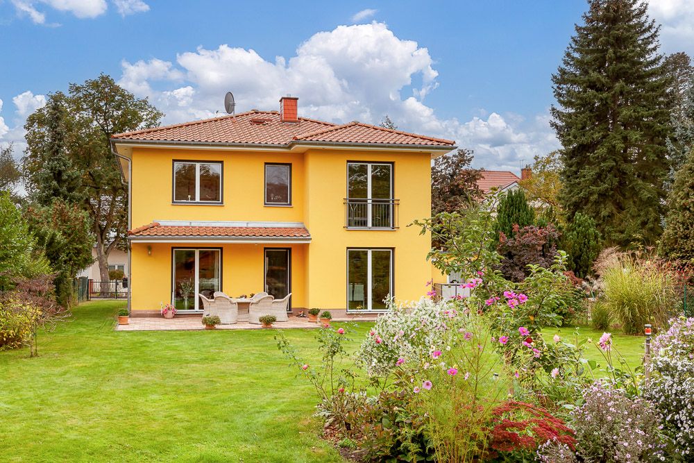 Modernes gelbes Wohnhaus mit Garten, Terrasse und vielen Blumen im Vordergrund.