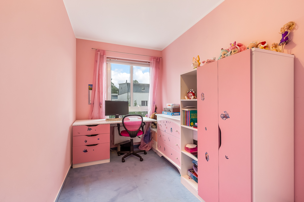 Kinderzimmer mit rosa Wänden, Schreibtisch, Stuhl, Schrank und Regal, Spielzeug darauf.