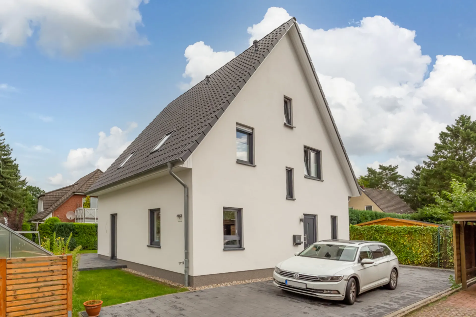 Modernes Einfamilienhaus mit Satteldach, grauen Fenstern und geparktem weißen Auto vor dem Haus.
