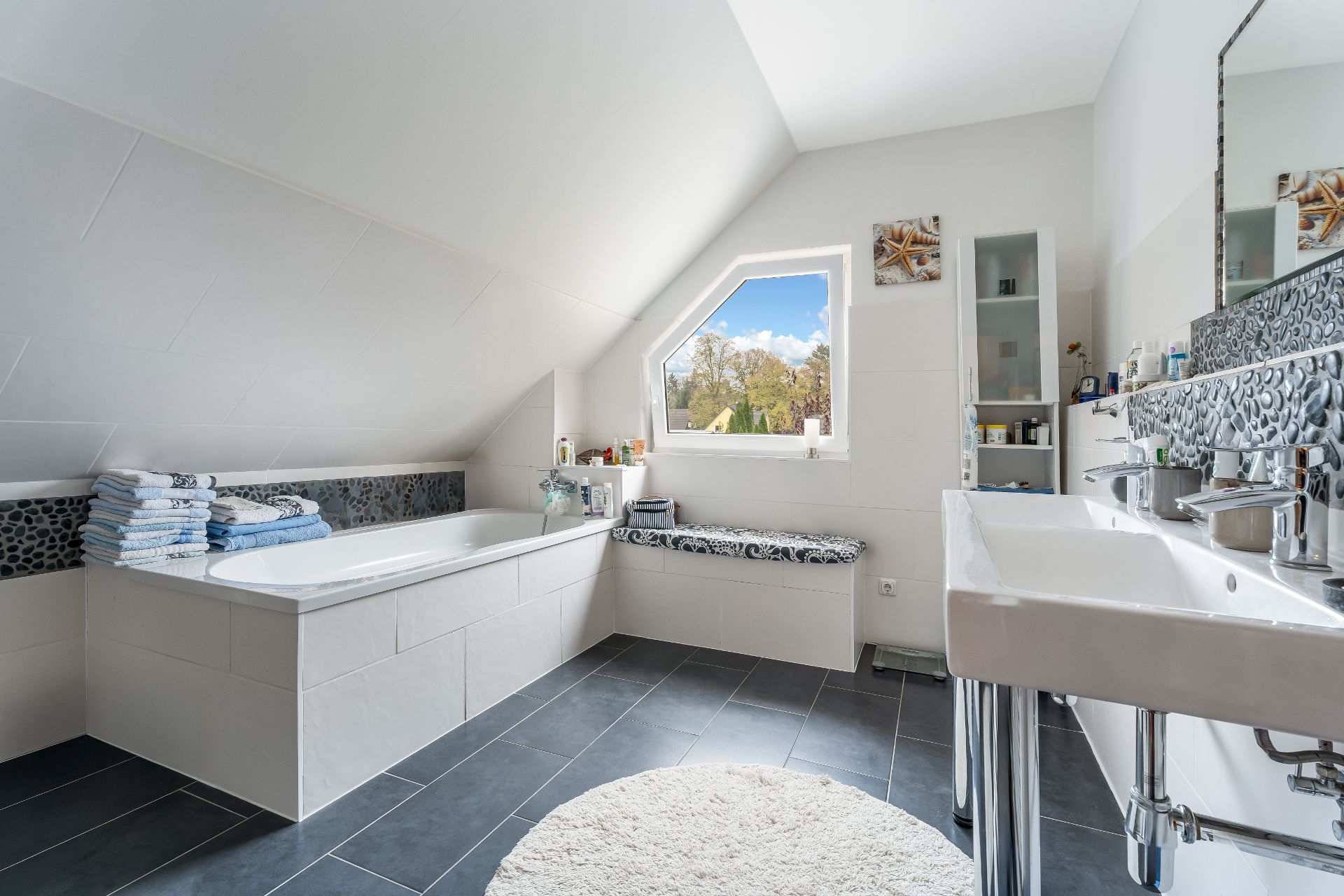 Modernes Badezimmer mit Badewanne, zwei Waschbecken, Fenster und gefliestem Boden.