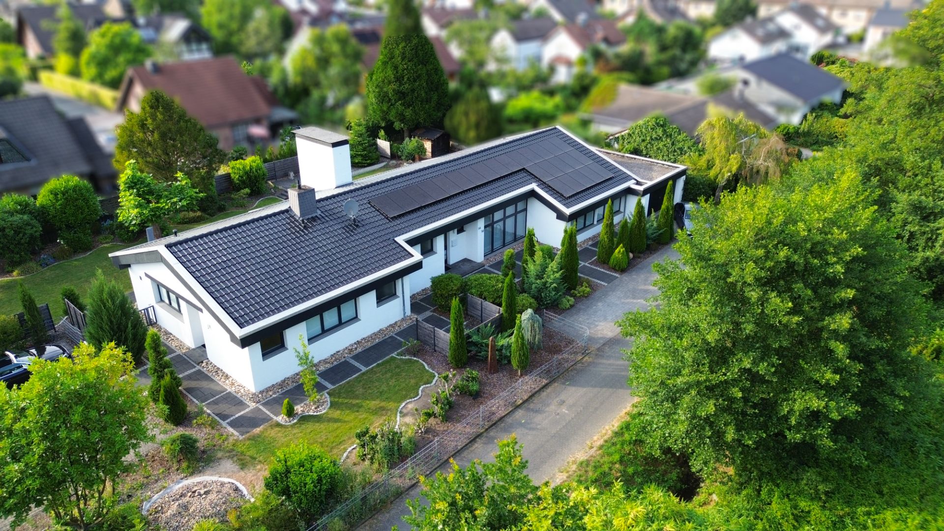 Luftaufnahme eines modernen Einfamilienhauses mit Solarpanels auf dem Dach und Garten.