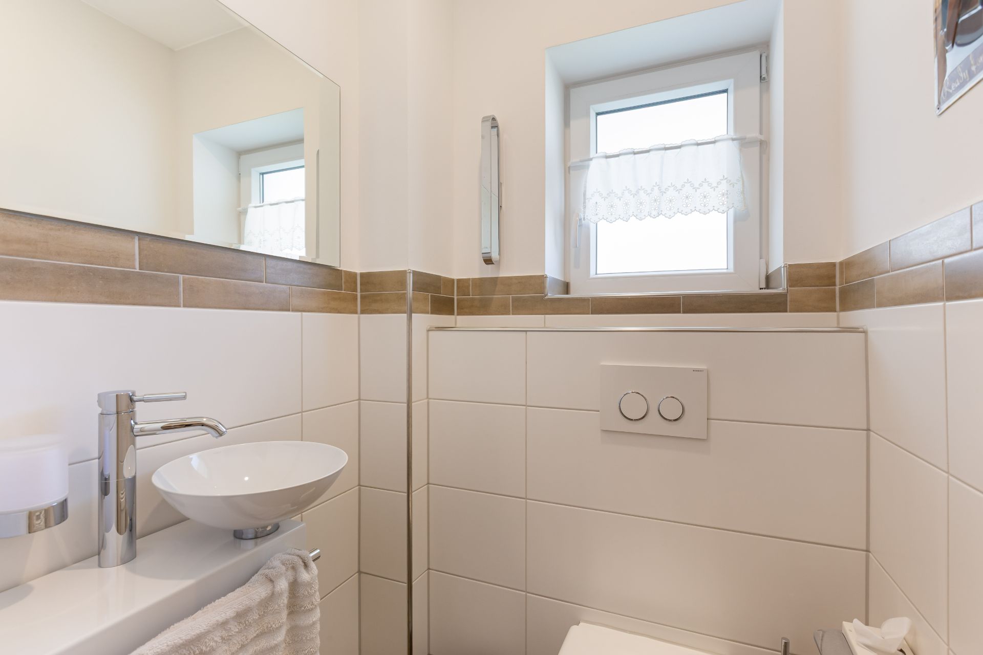Kleines Badezimmer mit Waschbecken, Spiegel, Fenster und Wandtoilette.