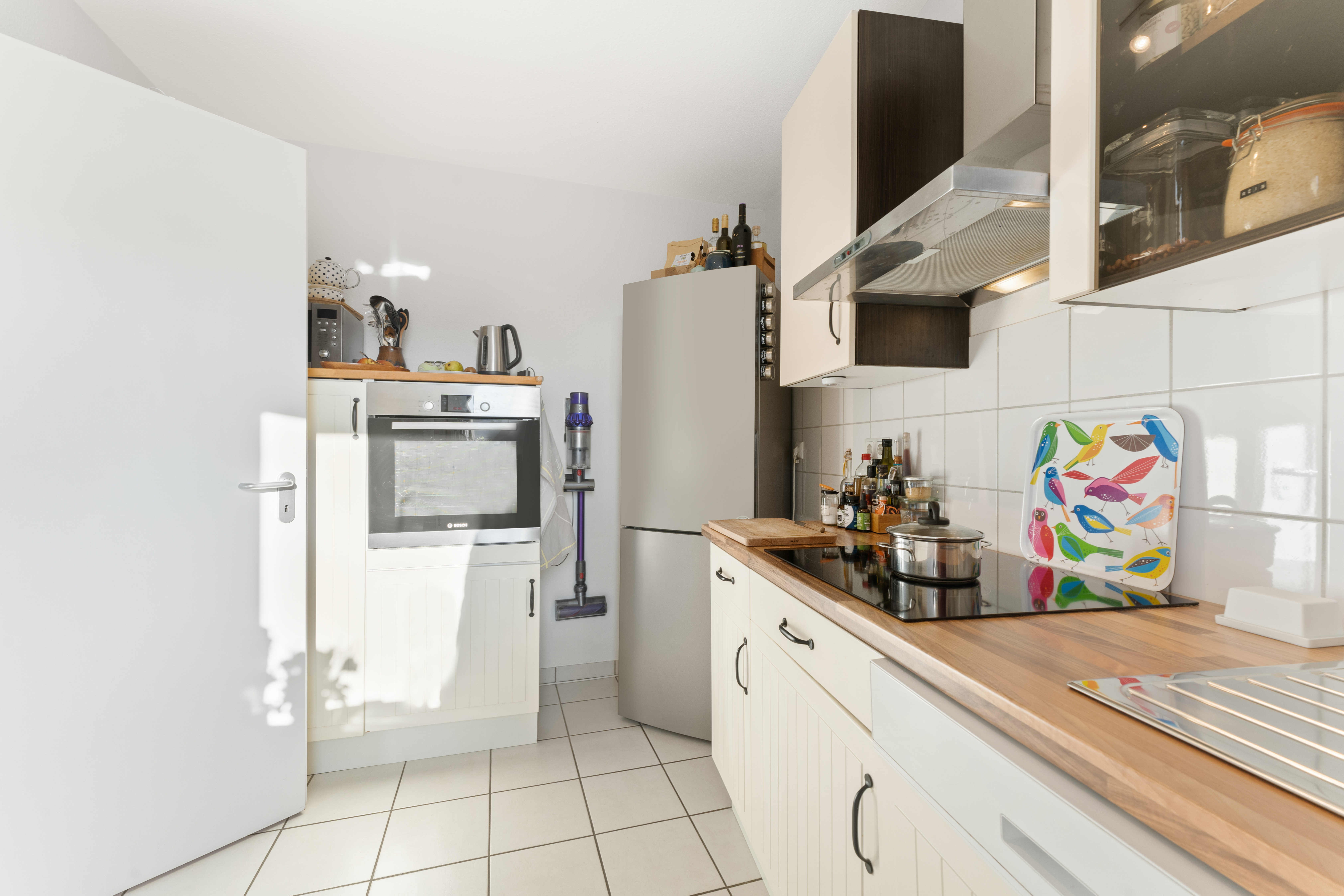 Moderne Küche mit Herd, Ofen, Kühlschrank und buntem Tablett mit Vogelmotiven auf der Arbeitsplatte.