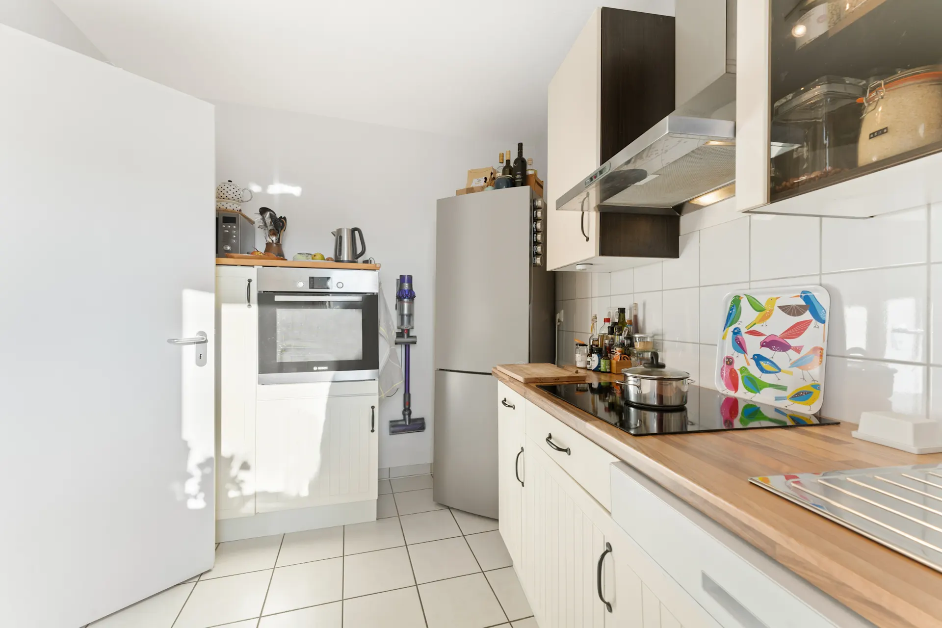 Moderne Küche mit Herd, Ofen, Kühlschrank und buntem Tablett mit Vogelmotiven auf der Arbeitsplatte.