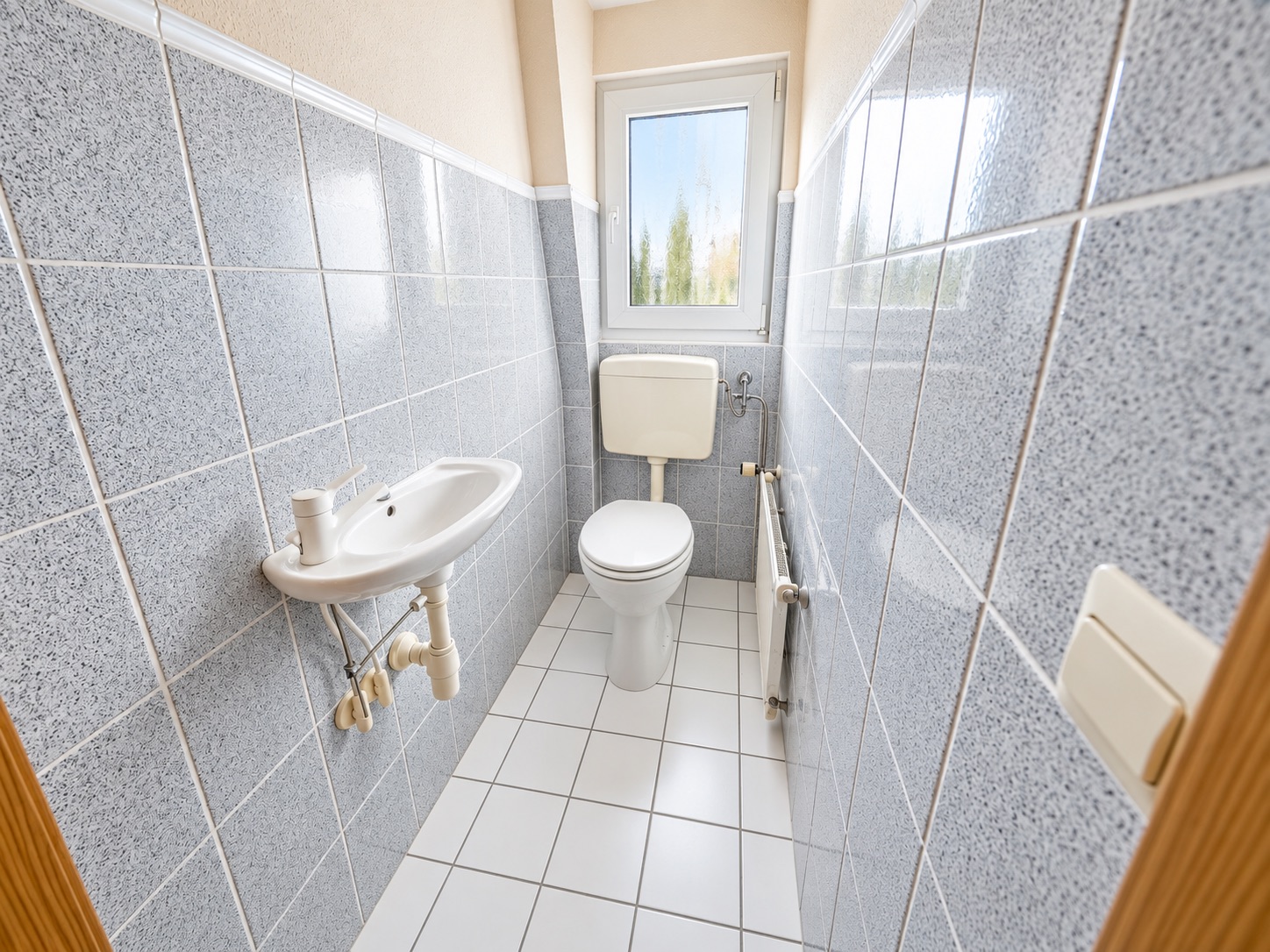 Schmales Badezimmer mit Toilette, kleinem Waschbecken und Fenster.