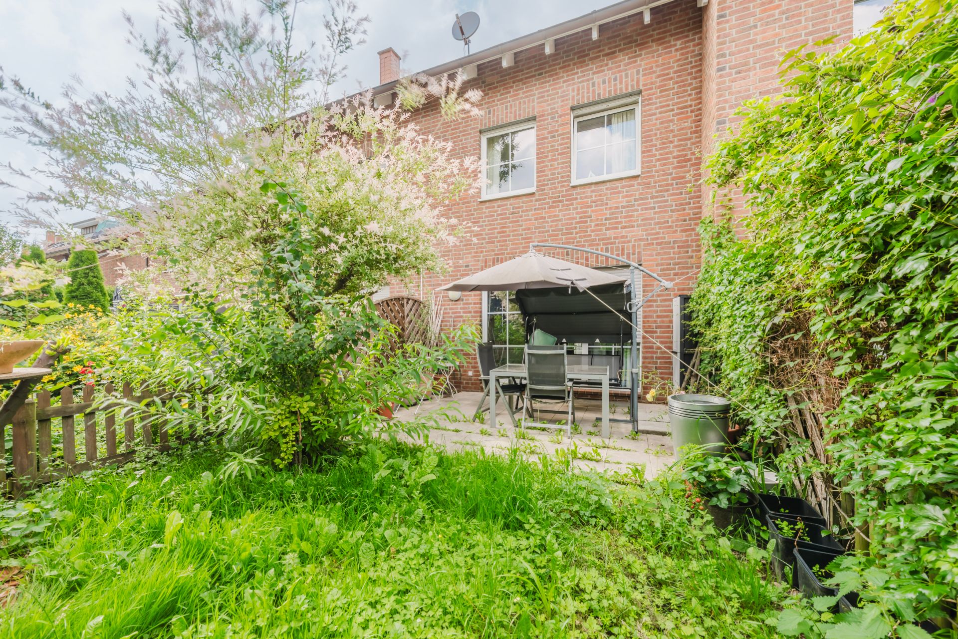 Garten mit Terrasse, Sitzgruppe und Sonnenschirm vor einem roten Backsteinhaus.