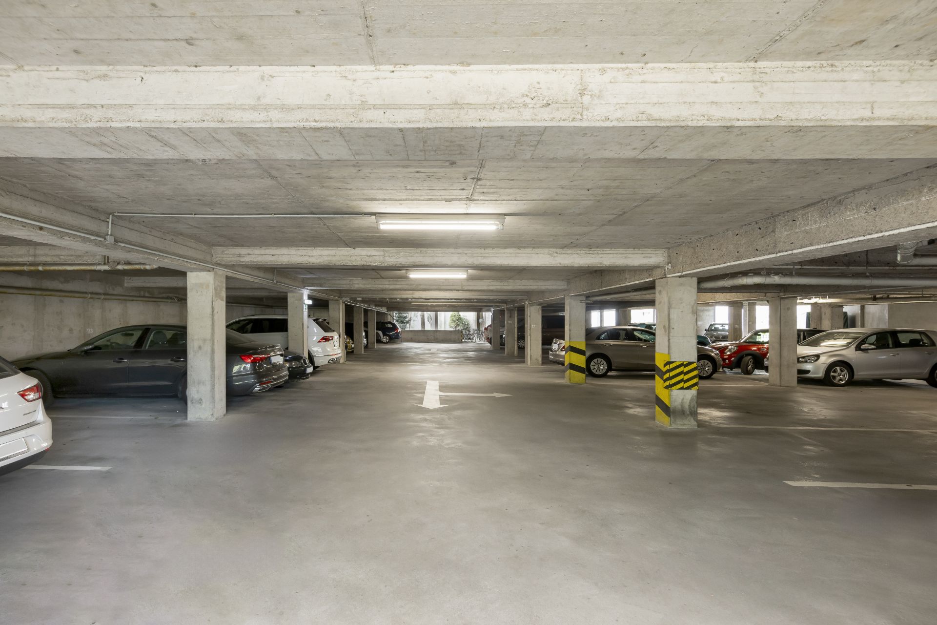 Helle Tiefgarage mit mehreren geparkten Autos und Betonpfeilern.