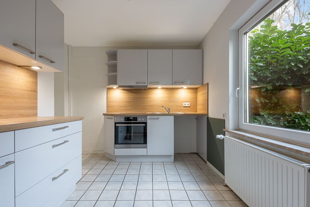 Moderne Einbauküche mit hellen Fronten, Holzarbeitsplatte und großem Fenster mit Blick ins Grüne.