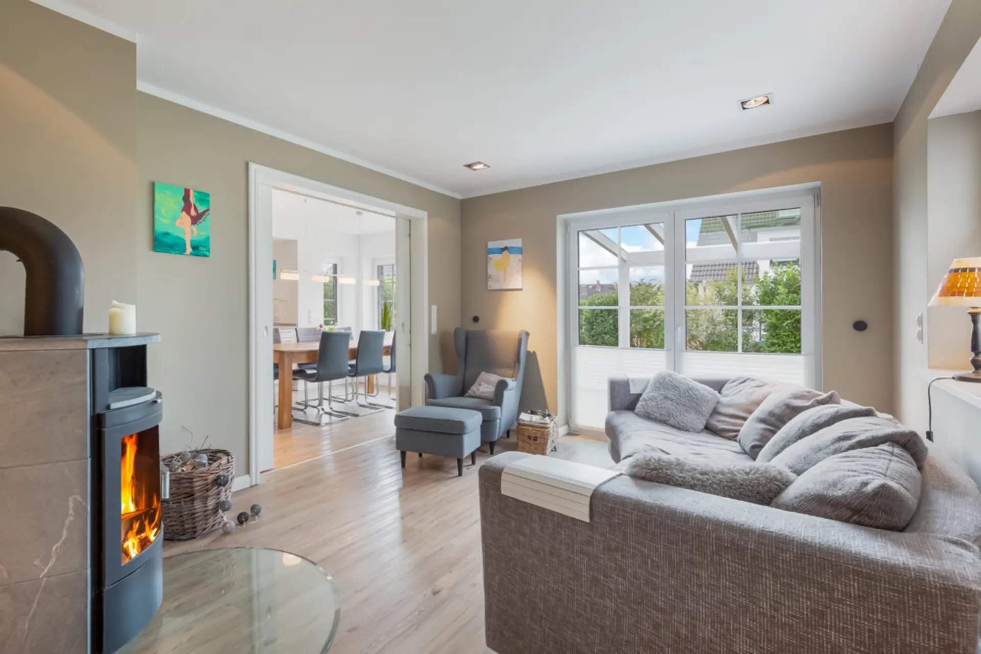 Helles Wohnzimmer mit Kamin, grauem Sofa, Sessel und Zugang zu Essbereich und Terrasse.