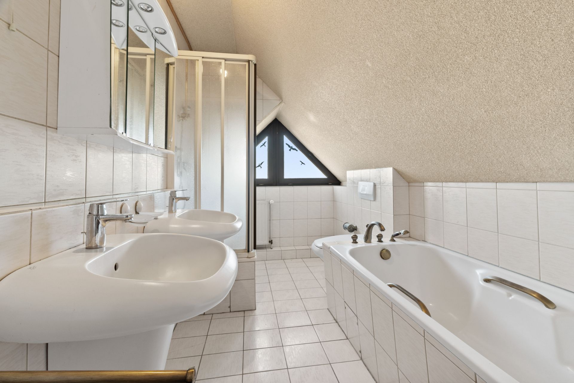 Helles Badezimmer mit zwei Waschbecken, Badewanne, Dusche und schrägem Dachfenster.