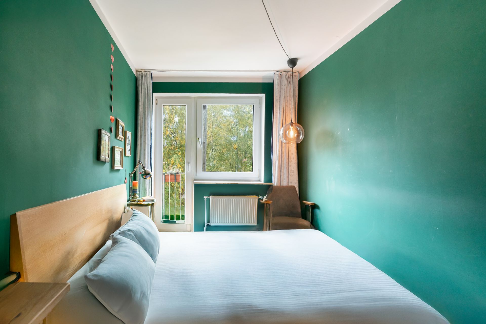 Schlafzimmer mit grün gestrichenen Wänden, Doppelbett, Fenster und Stuhl neben einem Heizkörper.