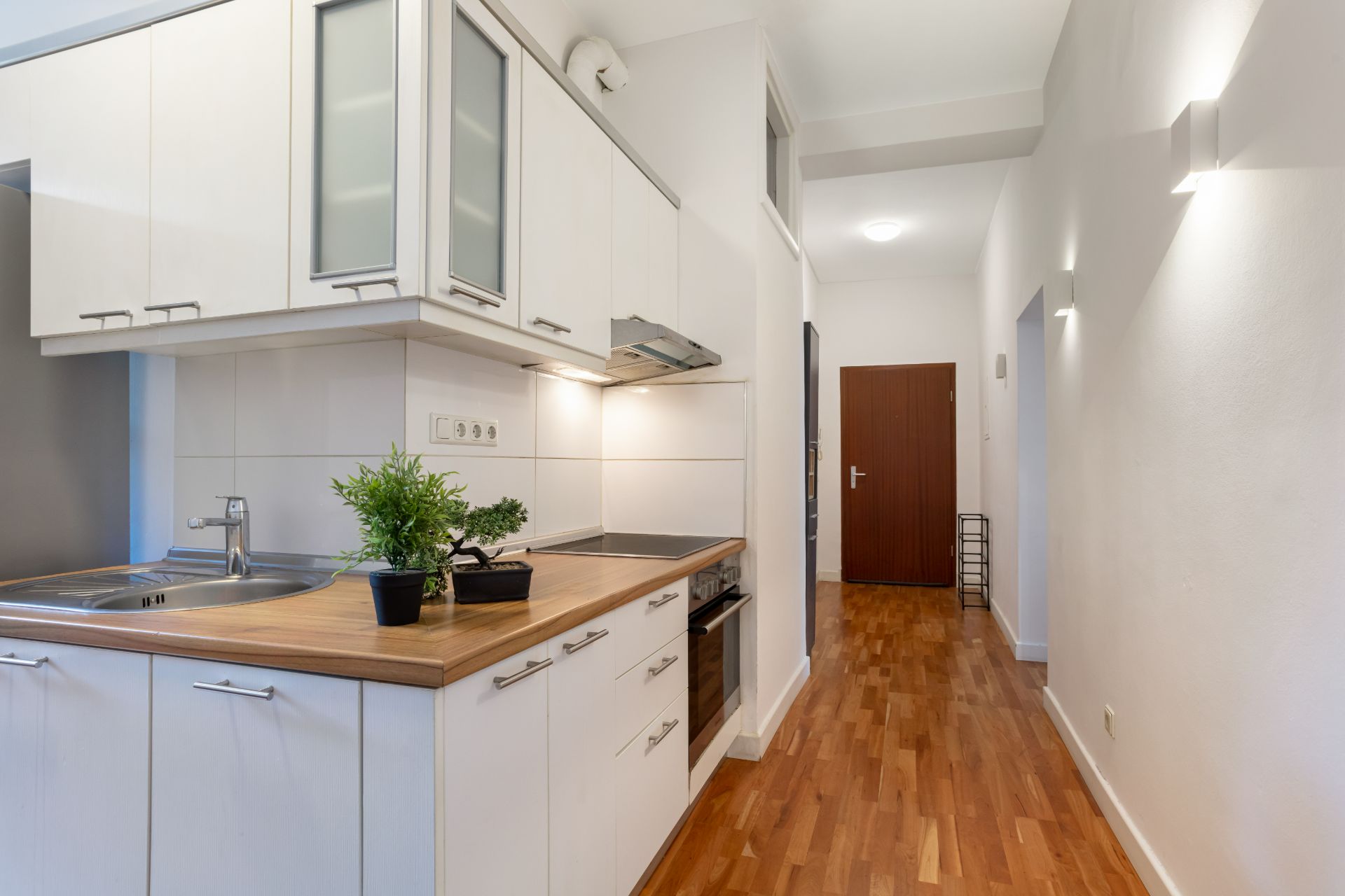 Moderne, weiße Einbauküche mit Holzarbeitsplatte in Flur mit Holzboden.