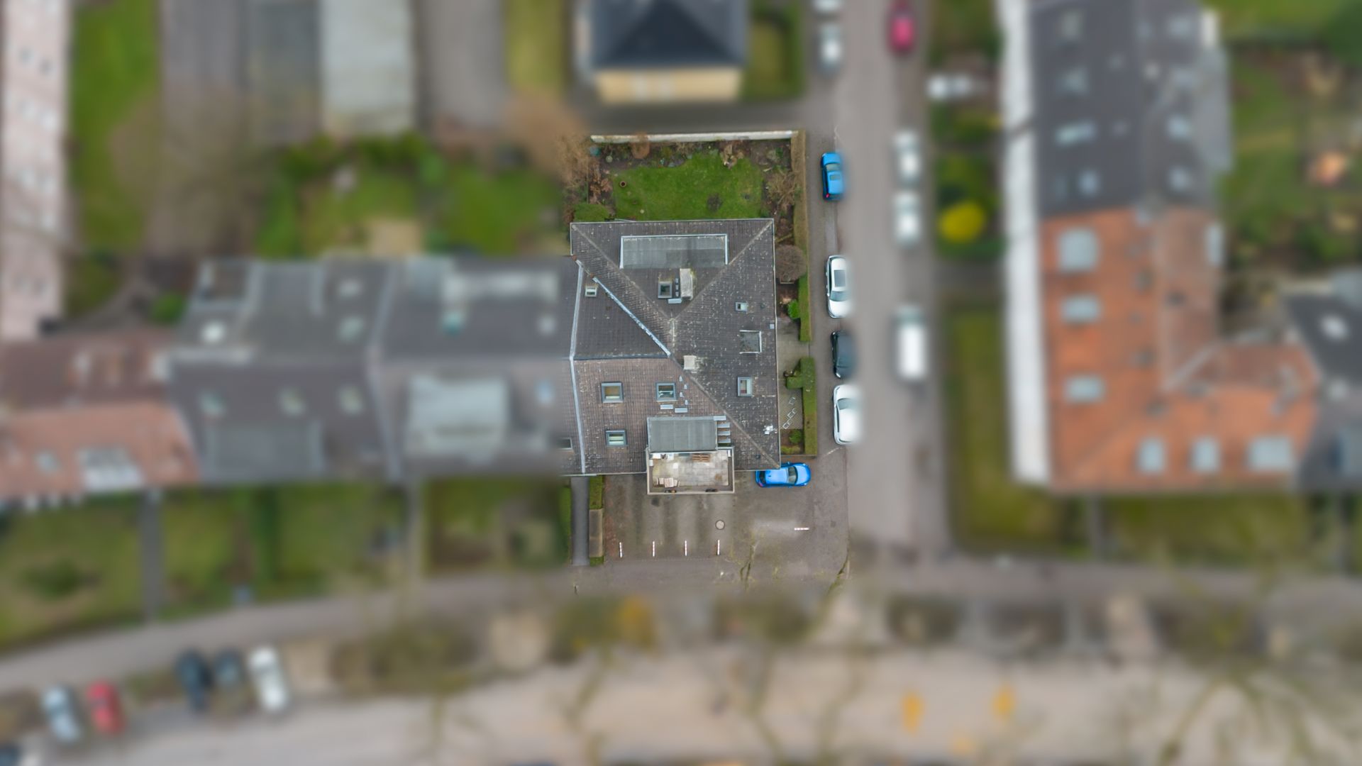 Luftaufnahme eines Wohnhauses mit angrenzendem Parkplatz und mehreren Autos.