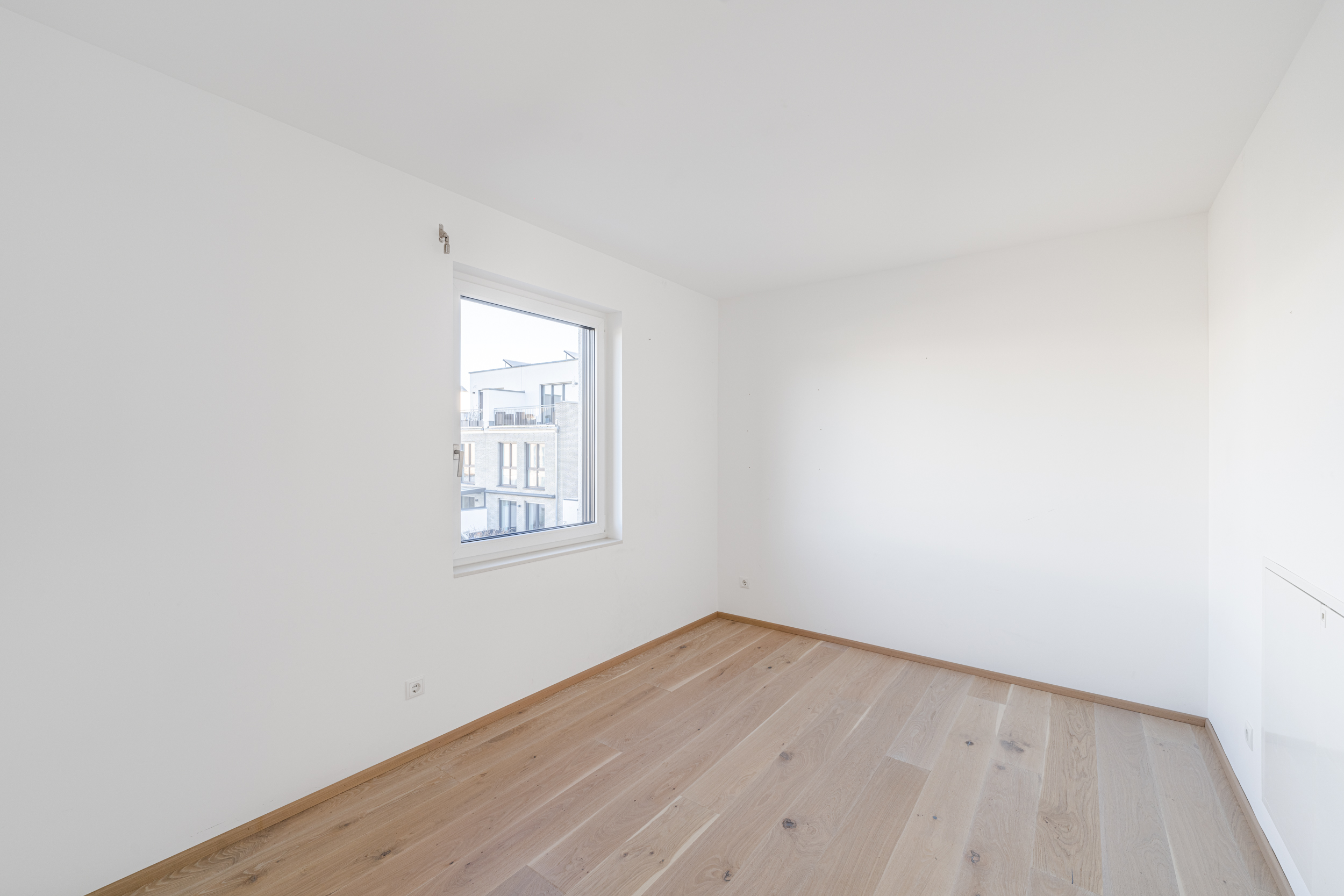 Leeres Zimmer mit weiß gestrichenen Wänden, Holzfußboden und einem Fenster.