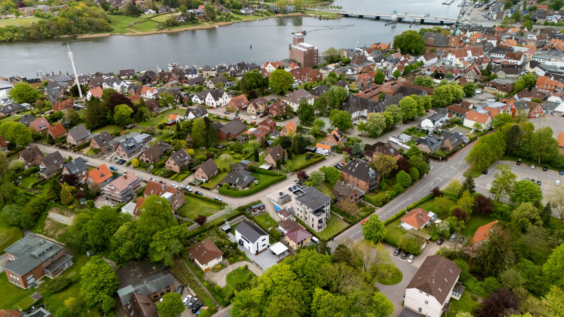 Luftaufnahme einer Wohnsiedlung mit vielen Häusern, Straßen und Bäumen nahe an einem Fluss.