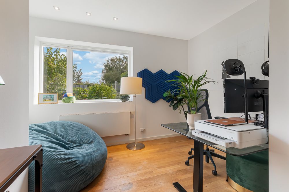 Helles Arbeitszimmer mit großem Fenster, Sitzsack, Schreibtisch, Monitor und Zimmerpflanze.