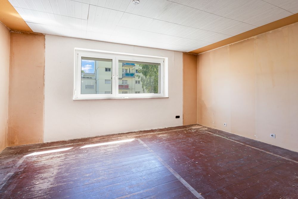 Leerer Raum mit großem Fenster, braunen Wänden und dunklem Boden.