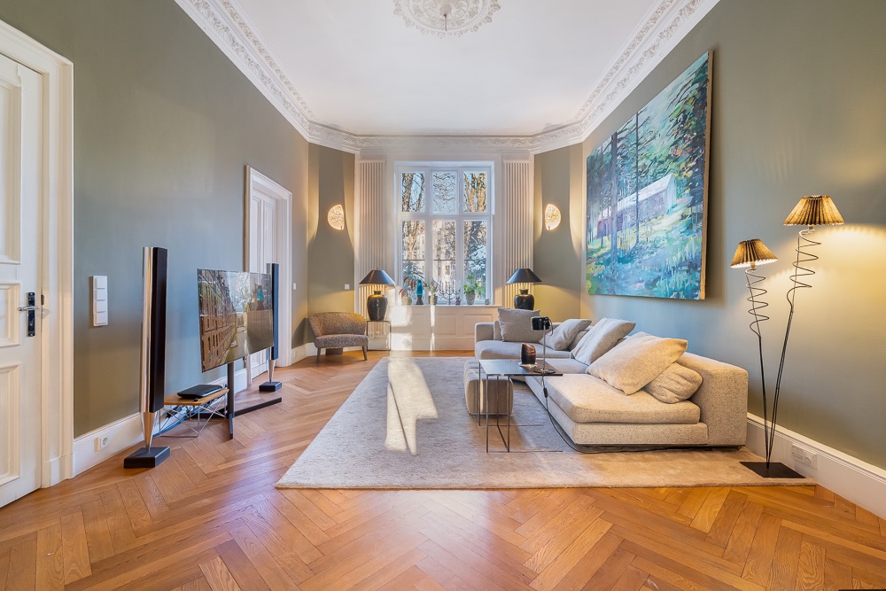 Helles Wohnzimmer mit großem Fenster, Sofa, Fernseher und modernem Gemälde an der Wand.