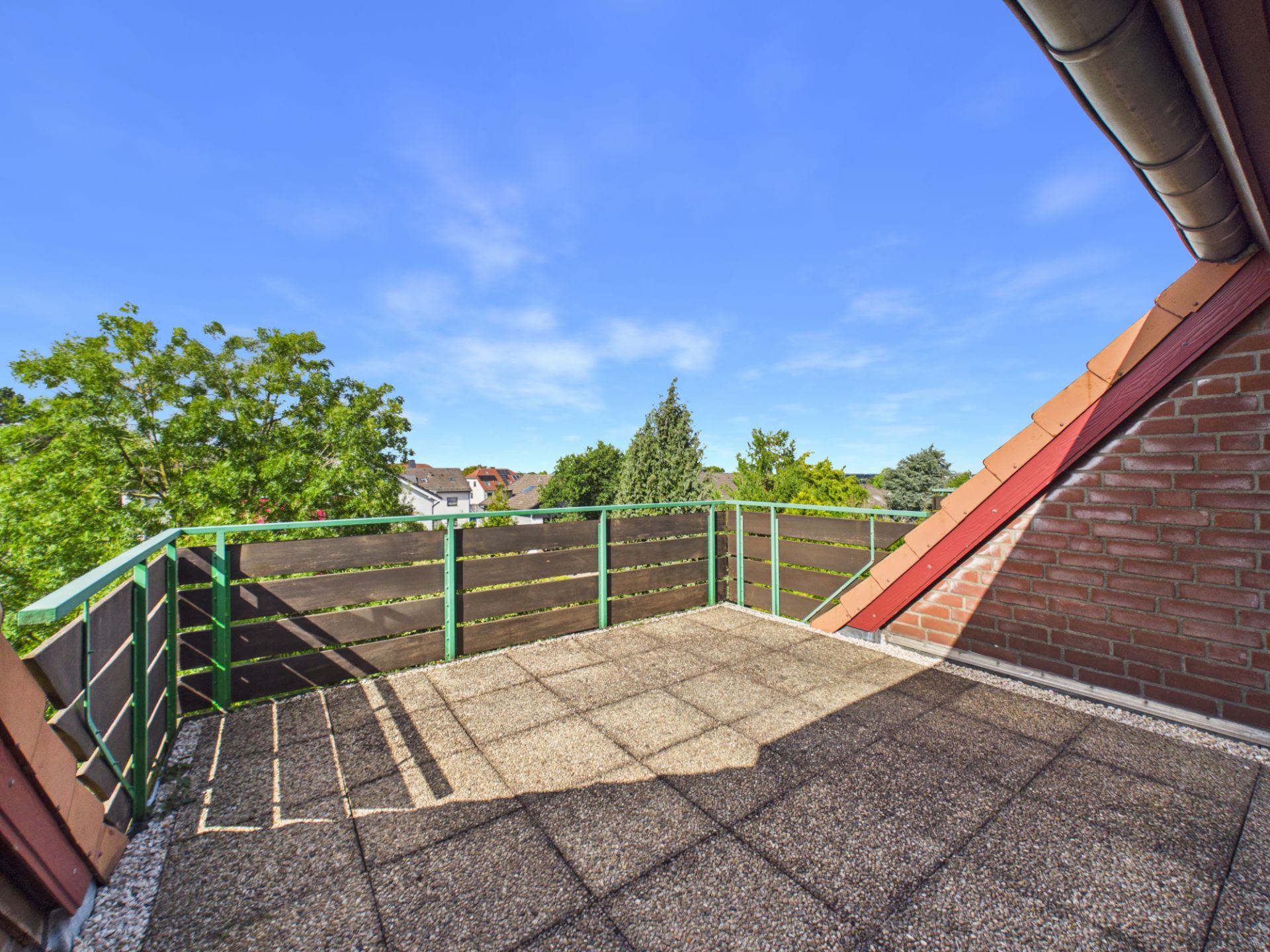 Dachterrasse mit Fliesenboden, seitlichen Ziegelwänden und Blick auf Bäume.