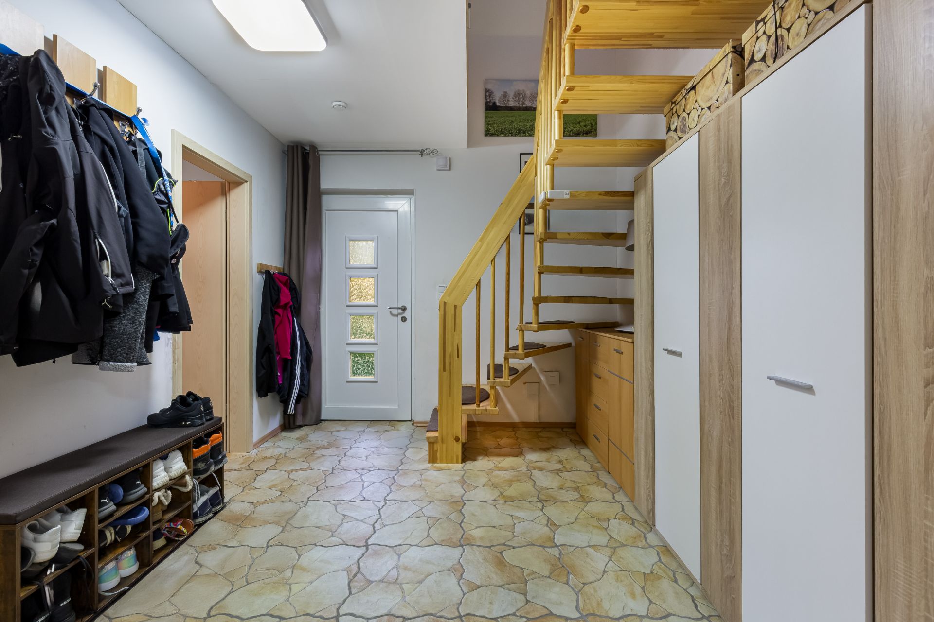 Flur in einem Wohnhaus mit Garderobe, Schuhregal, Treppe und weißen Türen.