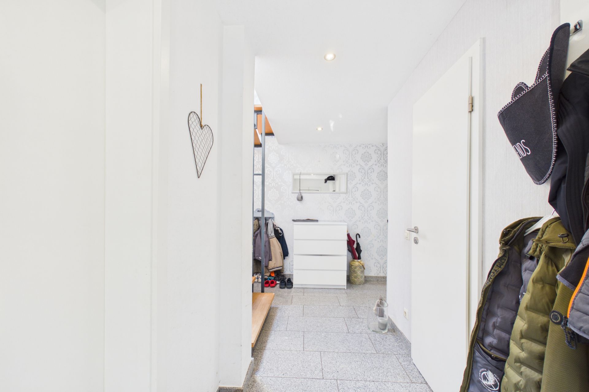 Heller Flur mit Garderobe, Kommode und Jacken an der Wand.