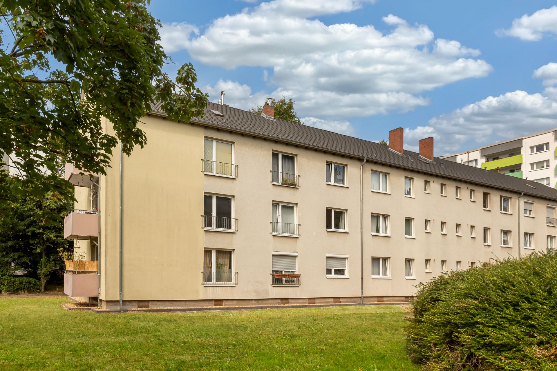 Dreistöckiges Wohnhaus mit mehreren Fenstern und umliegender Grünfläche.