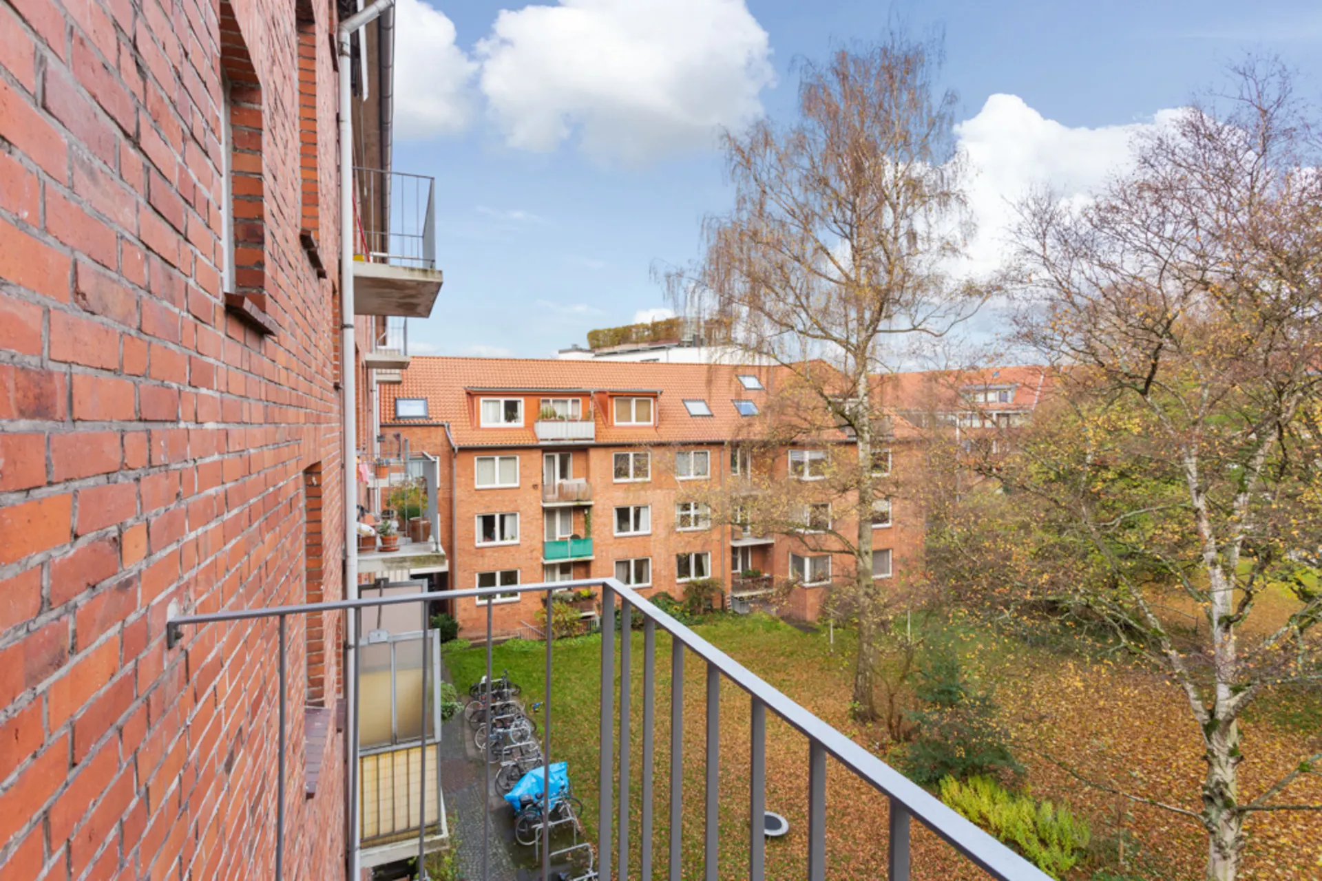 Blick von einem Balkon auf einen Innenhof mit Bäumen und angrenzenden Wohngebäuden aus rotem Backstein.