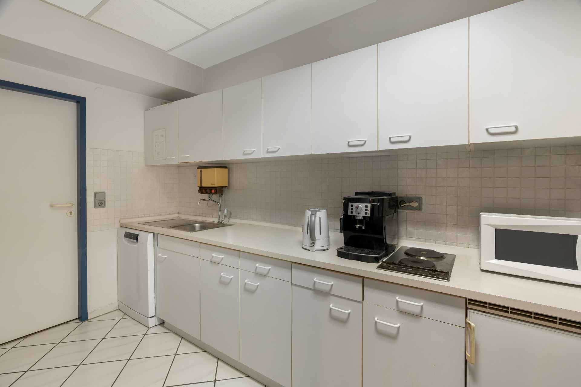 Weiße Einbauküche mit Kaffeemaschine, Wasserkocher, Mikrowelle und Herdplatten.