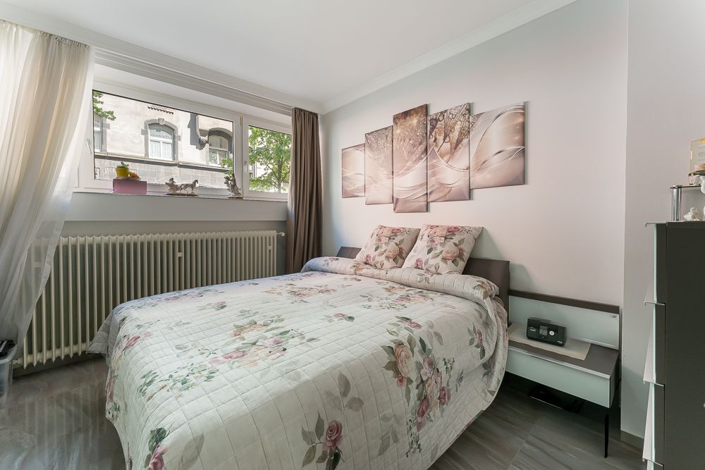 Helles Schlafzimmer mit Doppelbett, floralem Bettbezug und Bildern an der Wand.