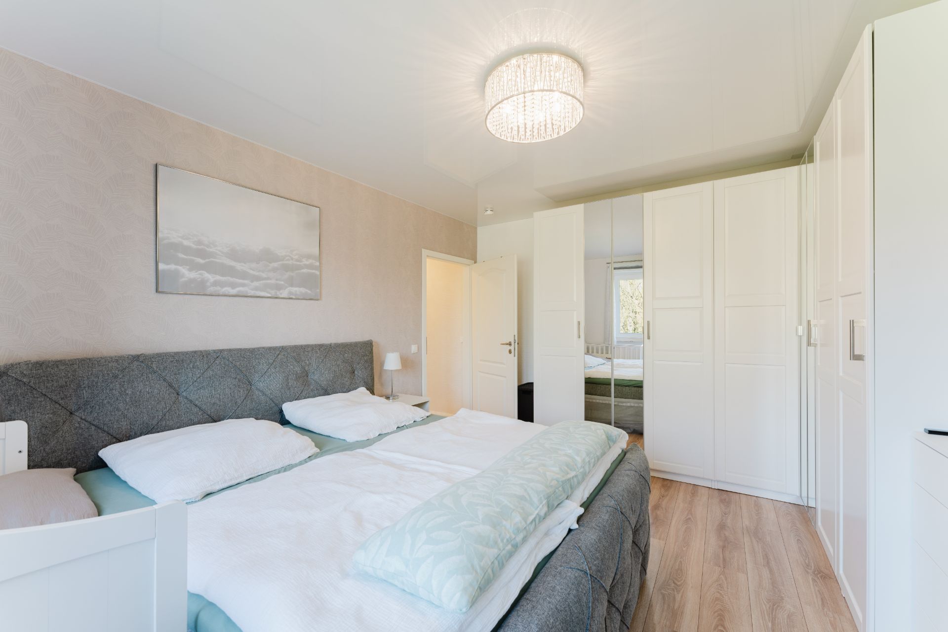 Helles Schlafzimmer mit Doppelbett, weißem Kleiderschrank und großem Fenster im Hintergrund.