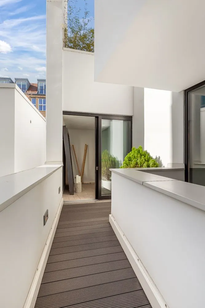 Moderner Balkon mit Holzboden, weißen Wänden und Glasschiebetür zu einer Wohnung.