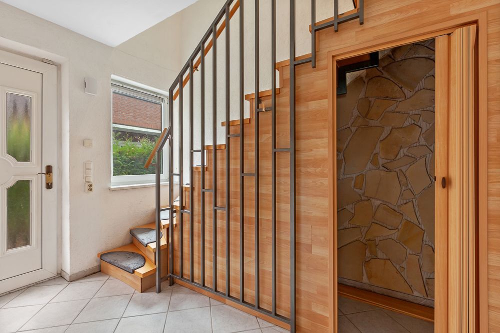 Heller Flur mit Treppe, Fenster und Tür zu einem Raum mit Steinwand.