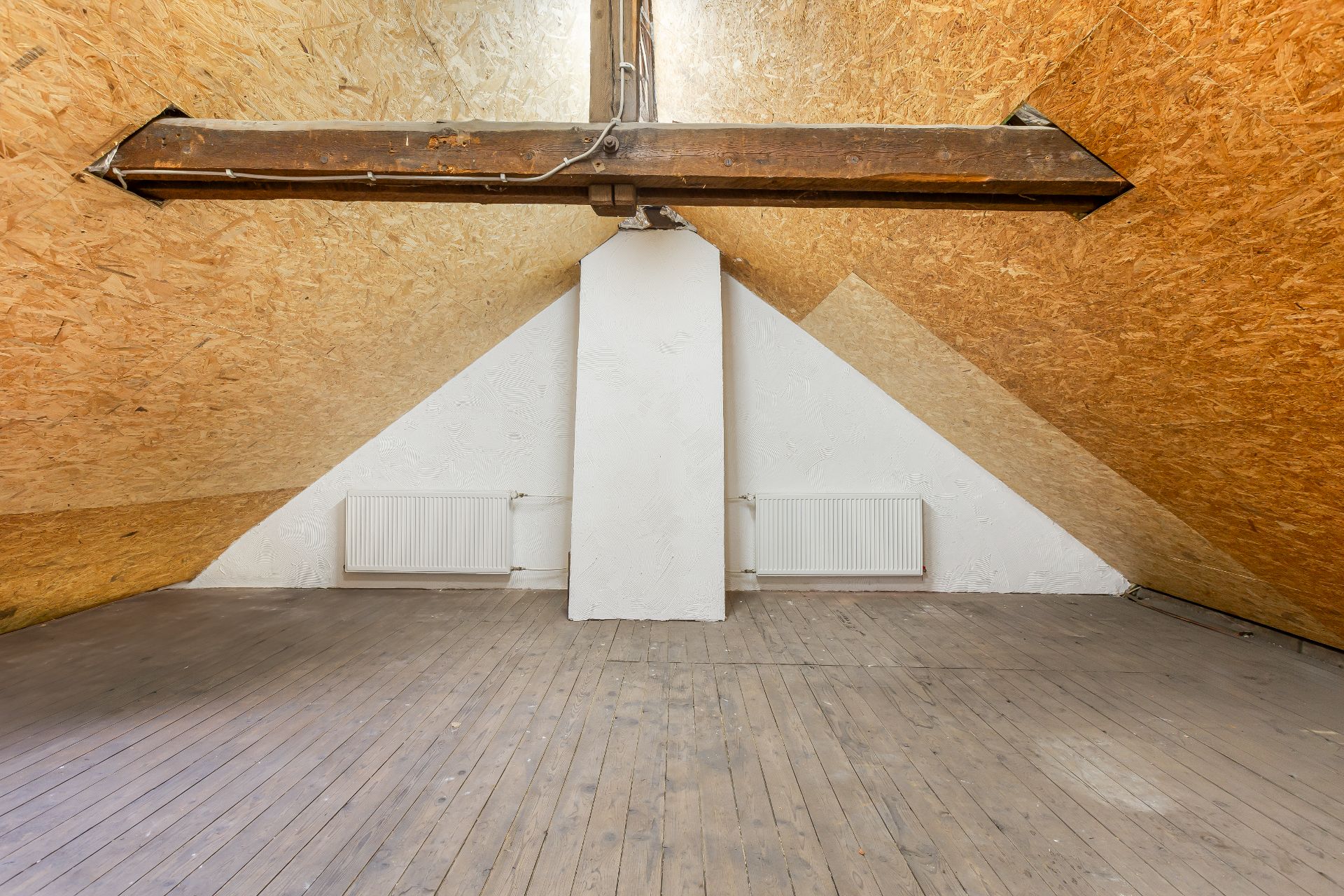 Leerer Dachboden mit Holzfußboden, sichtbaren Balken und zwei Heizkörpern an der Wand.