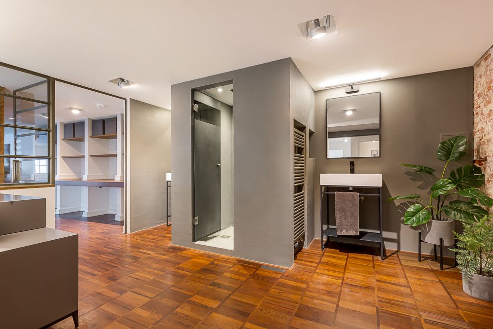 Modernes Badezimmer mit Waschbecken, Spiegel, Dusche, Pflanzen und Holzfußboden.