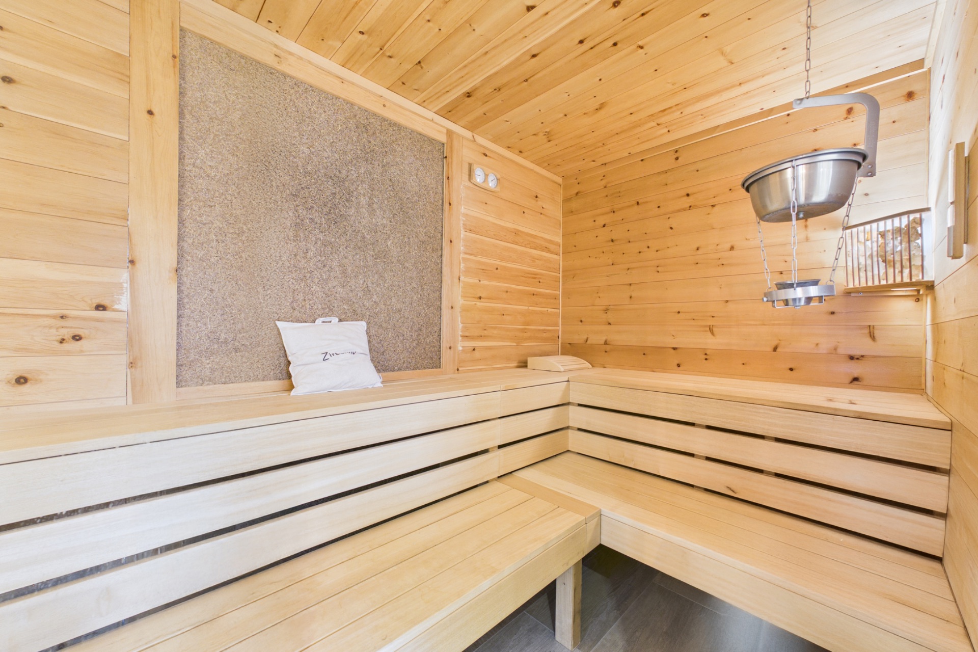 Helle Holzsauna mit zwei Bänken und einem Aufgusseimer an der Decke.
