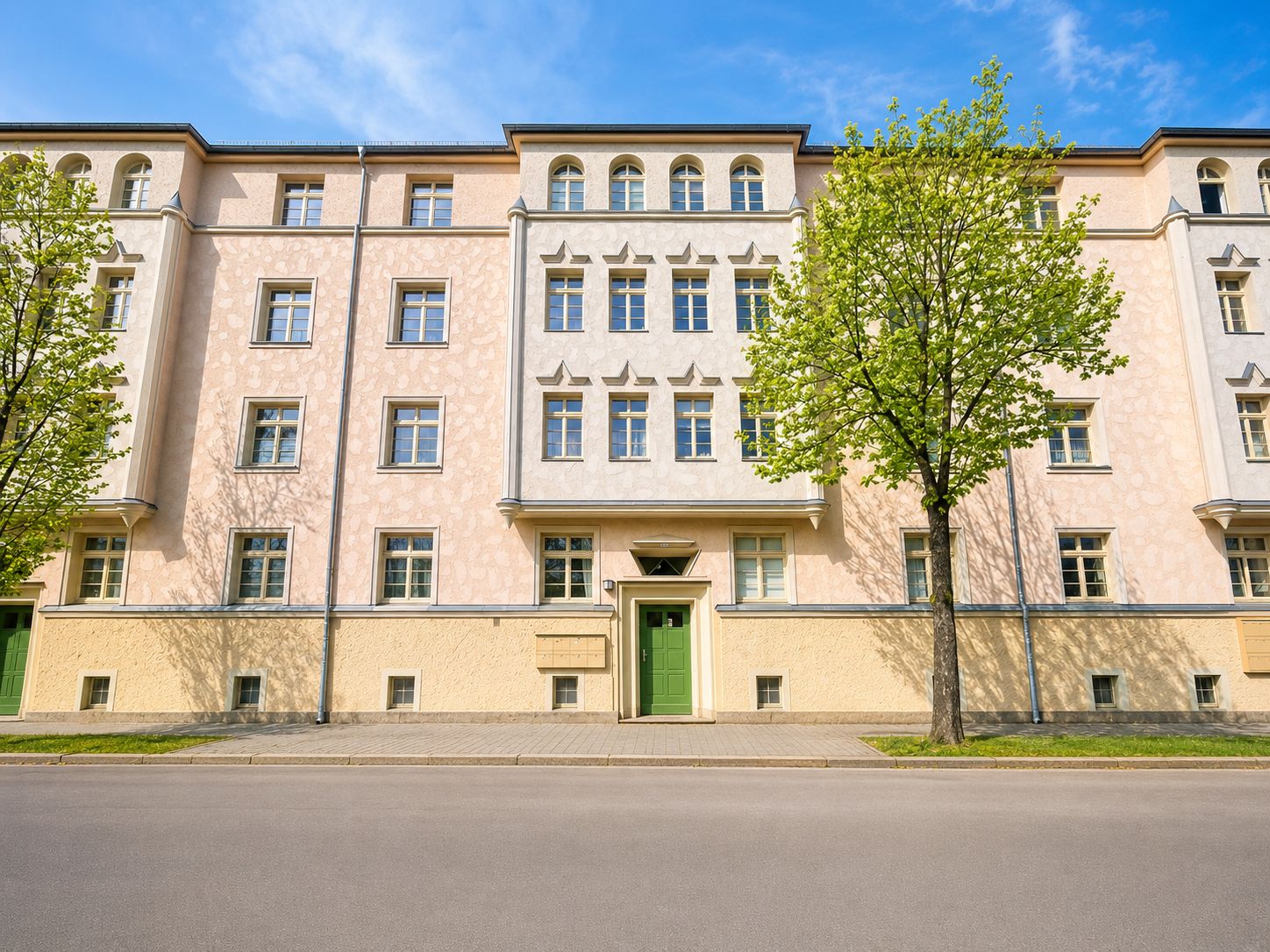 Wohnhaus mit heller Fassade, grüner Tür und Bäumen davor, aufgenommen bei Tageslicht.