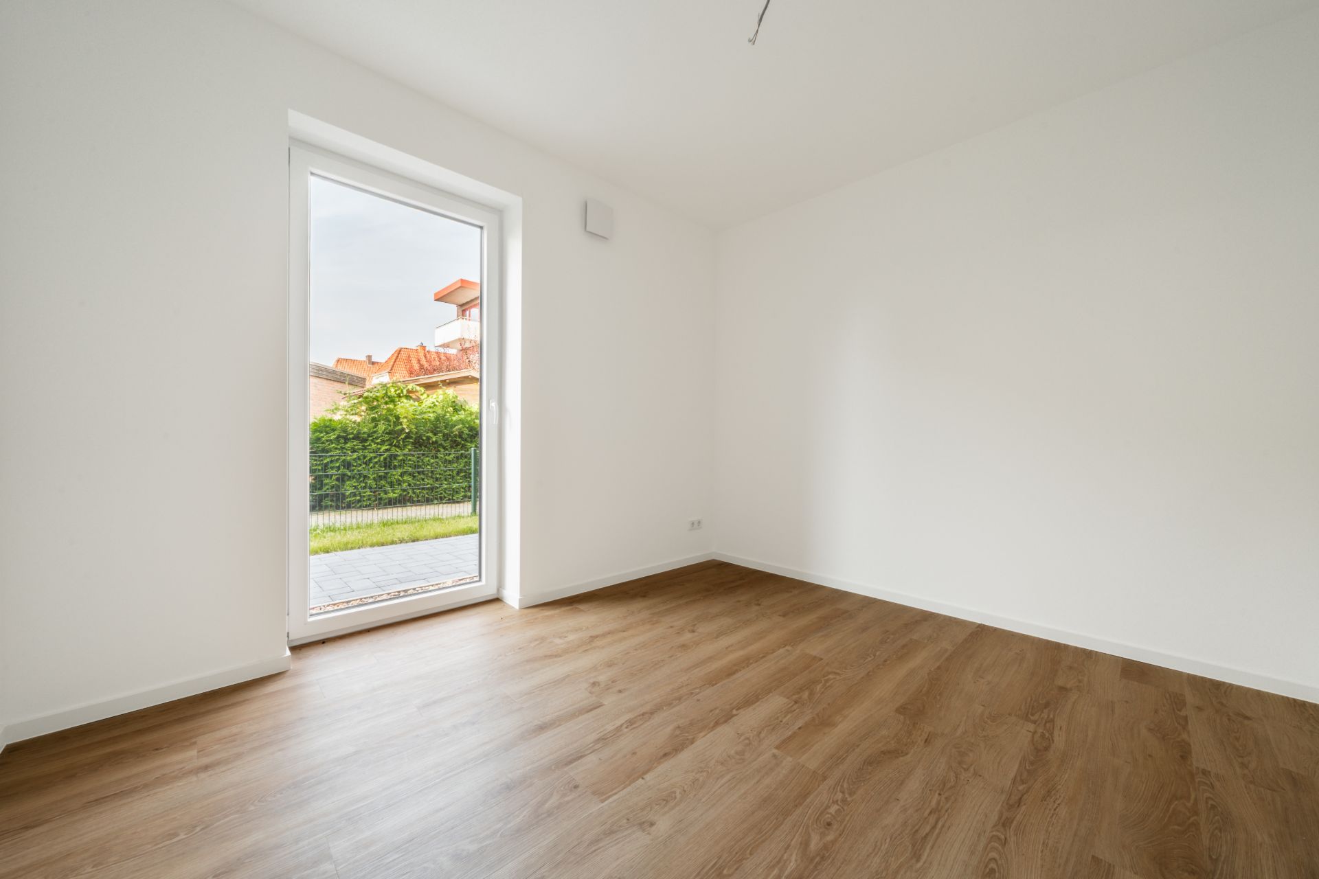 Leerzimmer mit Holzfußboden und großem Fenster zur Terrasse.