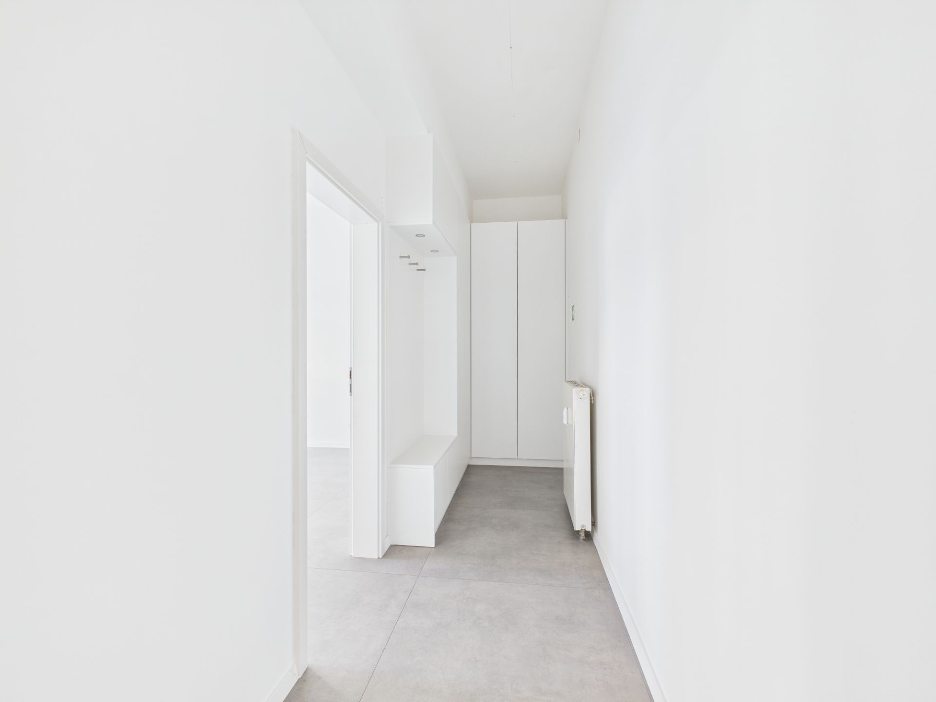 Heller Flur mit grauem Boden, weißen Wänden, Einbauschrank und Heizkörper.