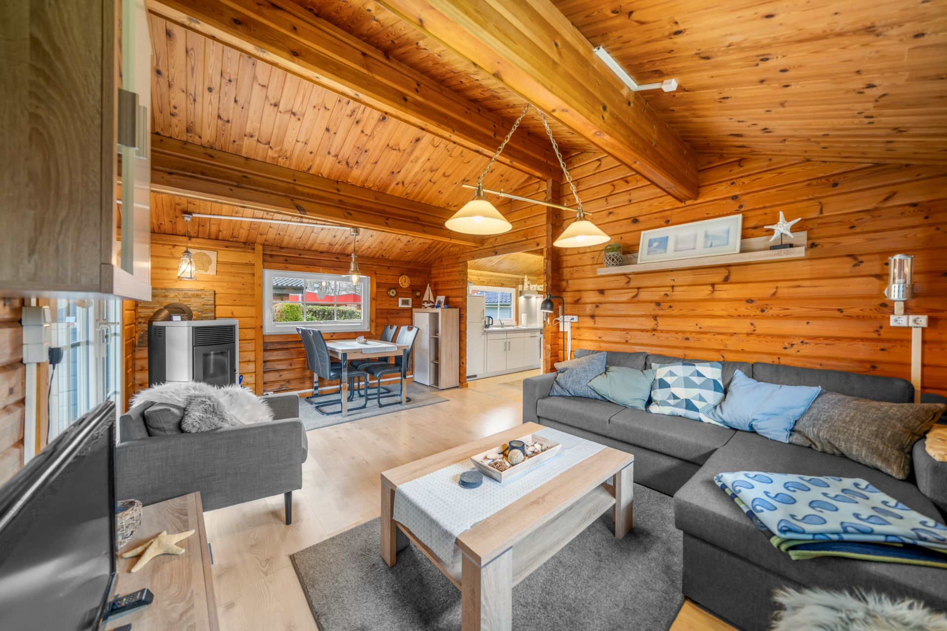 Gemütliches Wohnzimmer aus Holz mit Sofa, Couchtisch und Blick auf Essbereich und Küche.