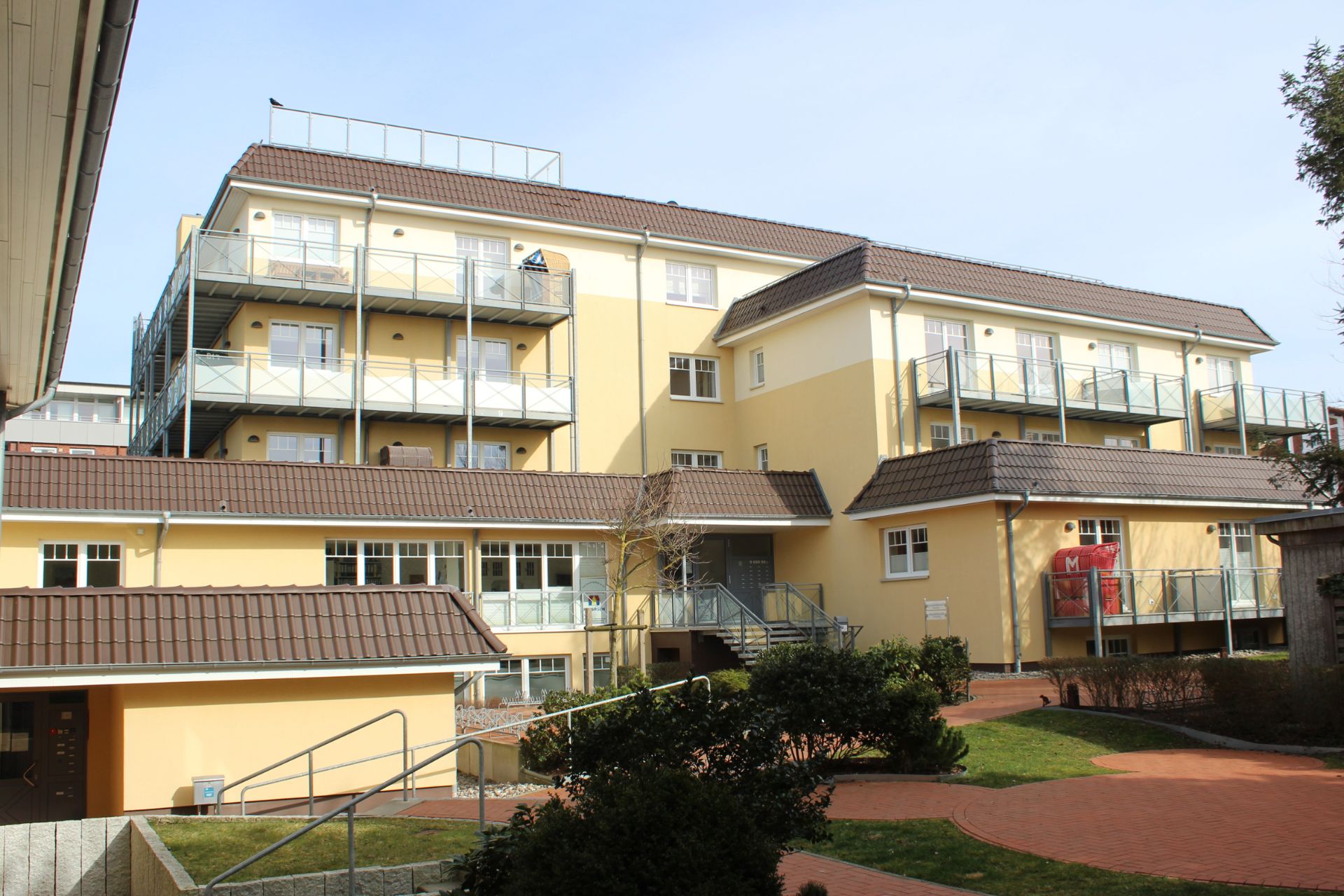 Gelbes Wohngebäude mit mehreren Balkonen und einem gepflegten Hof im Vordergrund.